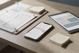 Smartphone, tablette et croquis d'écrans posés sur un bureau pendant la conception d'une application mobile